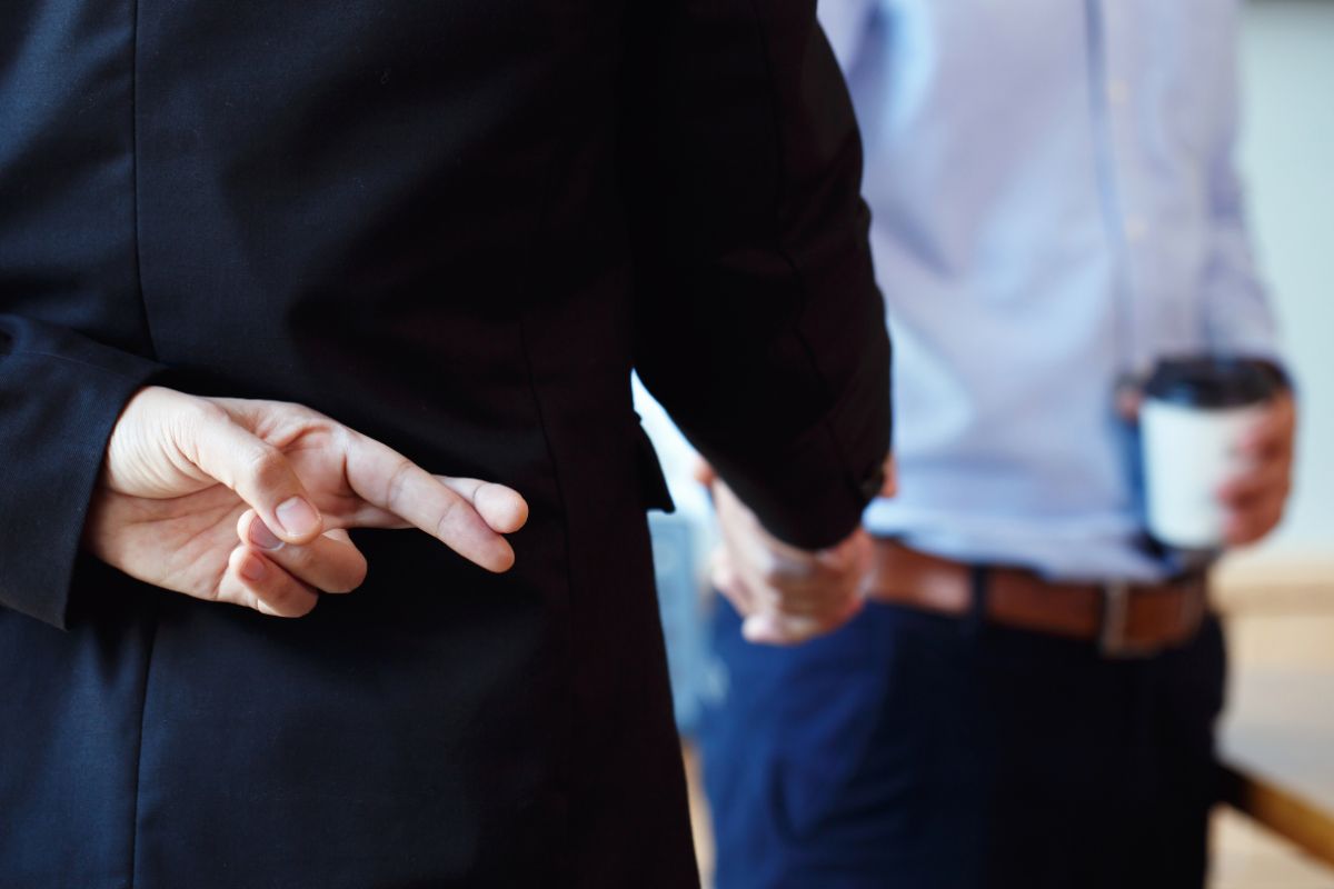 Uomo che incrocia le dita mentre da la mano ad un altra persona come simbolo di bugia