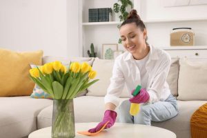 Donna felice con guanti fucsia, detersivo spray e panno che pulisce tavolino. Centrotavola con tulipani gialli