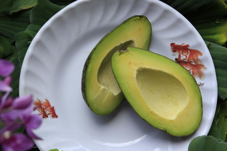 avocado senza nocciolo tagliato a metà sopra un piatto con dei fiori intorno