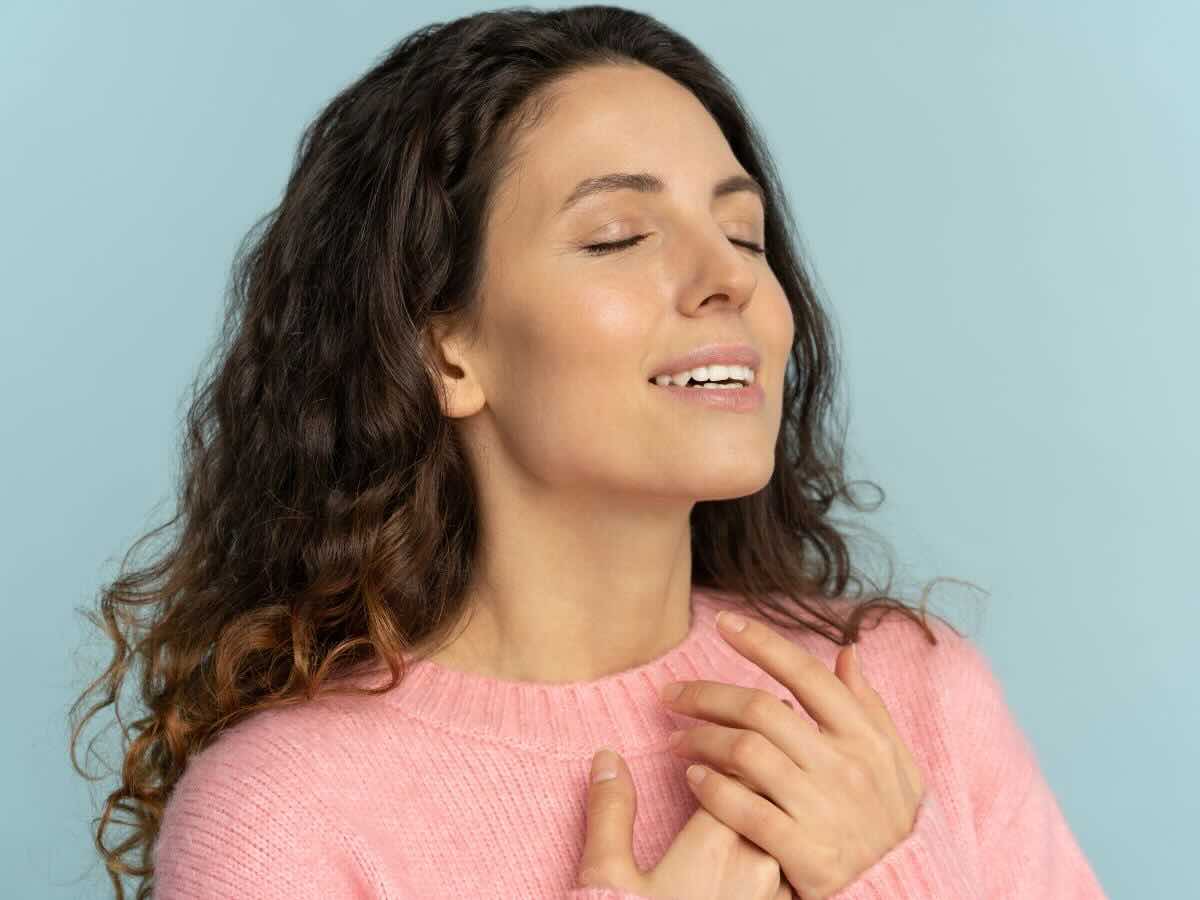 Donna con maglione rosa, occhi chiusi e mano sul petto, sorridente