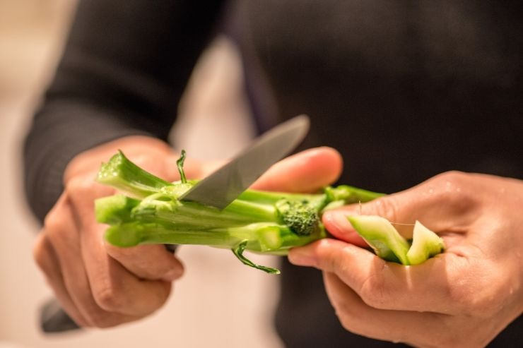 Mani che tagliano gambo del broccolo con il coltello