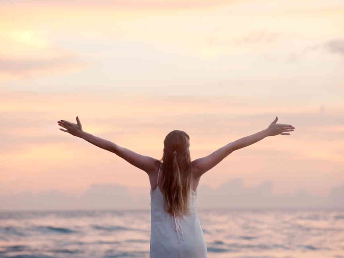 Ragazza felice a braccia aperte che guarda il mare