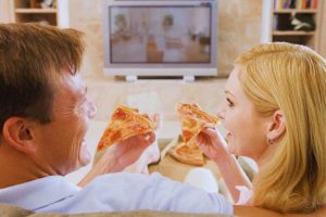 Coppia che mangia pizza davanti alla tv